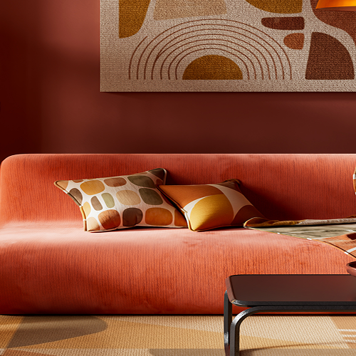 Retro woonkamer met een oranje fluwelen bank, gepatroonde kussens en een plaid, een ronde vloerlamp met rieten kap, donkerhouten kast en een abstract kunstwerk met booglijnen boven de bank.