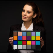 Een afbeelding van de Calibrite ColorChecker Classic die door het onderwerp in een portret wordt vastgehouden. De kleurreferentiekaart kan door fotografen worden gebruikt als referentie om te voorspellen en te controleren hoe kleur eruit zal zien onder verschillende lichtomstandigheden en om een nauwkeurige kleurweergave tijdens het bewerken te waarborgen. Het toont 24 vierkanten, elk met een kleurreferentie.